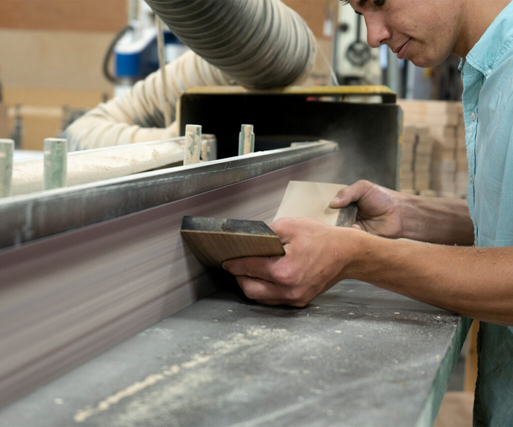 Woodworker sands hardwood board edge on a wide belt sander.