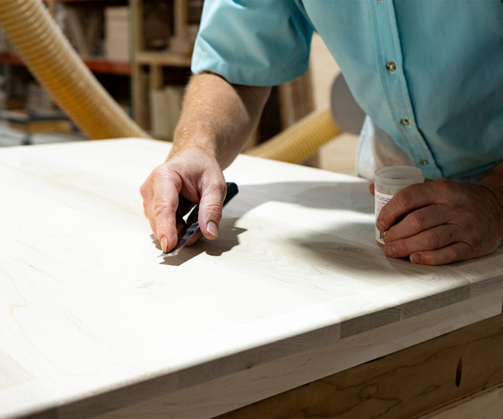 Woodworker scrapes solid hardwood tabletop to prep for finishing.