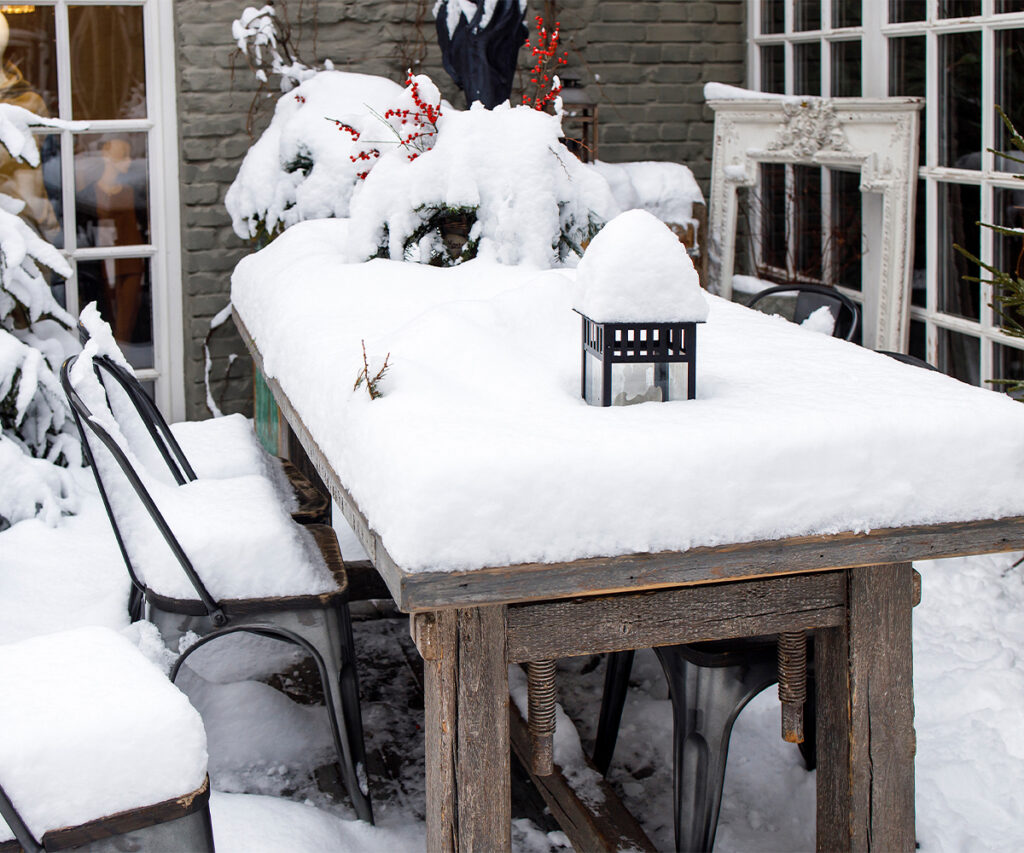 Snow-covered patio table and chairs showing outdoor furniture for winter damage.