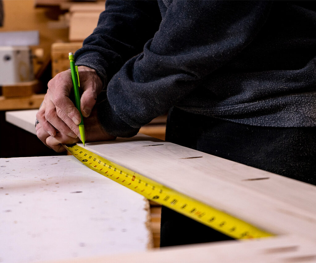 Craftsman measures a hardwood board and marks a cut line in a woodshop.